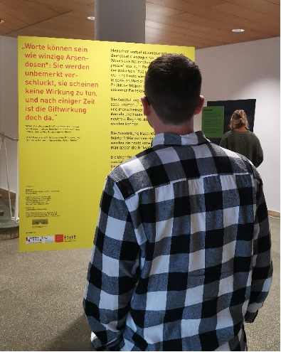 Ein Besucher ist von hinten zu sehen, wie er einen längeren Text auf einer der Tafeln liest.
