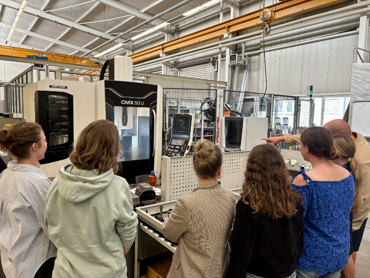 Das Bild zeigt eine Gruppe Referendarinnen, die zusammen mit ihrem Fachleiter eine CNC-Fräsmaschine begutachten
