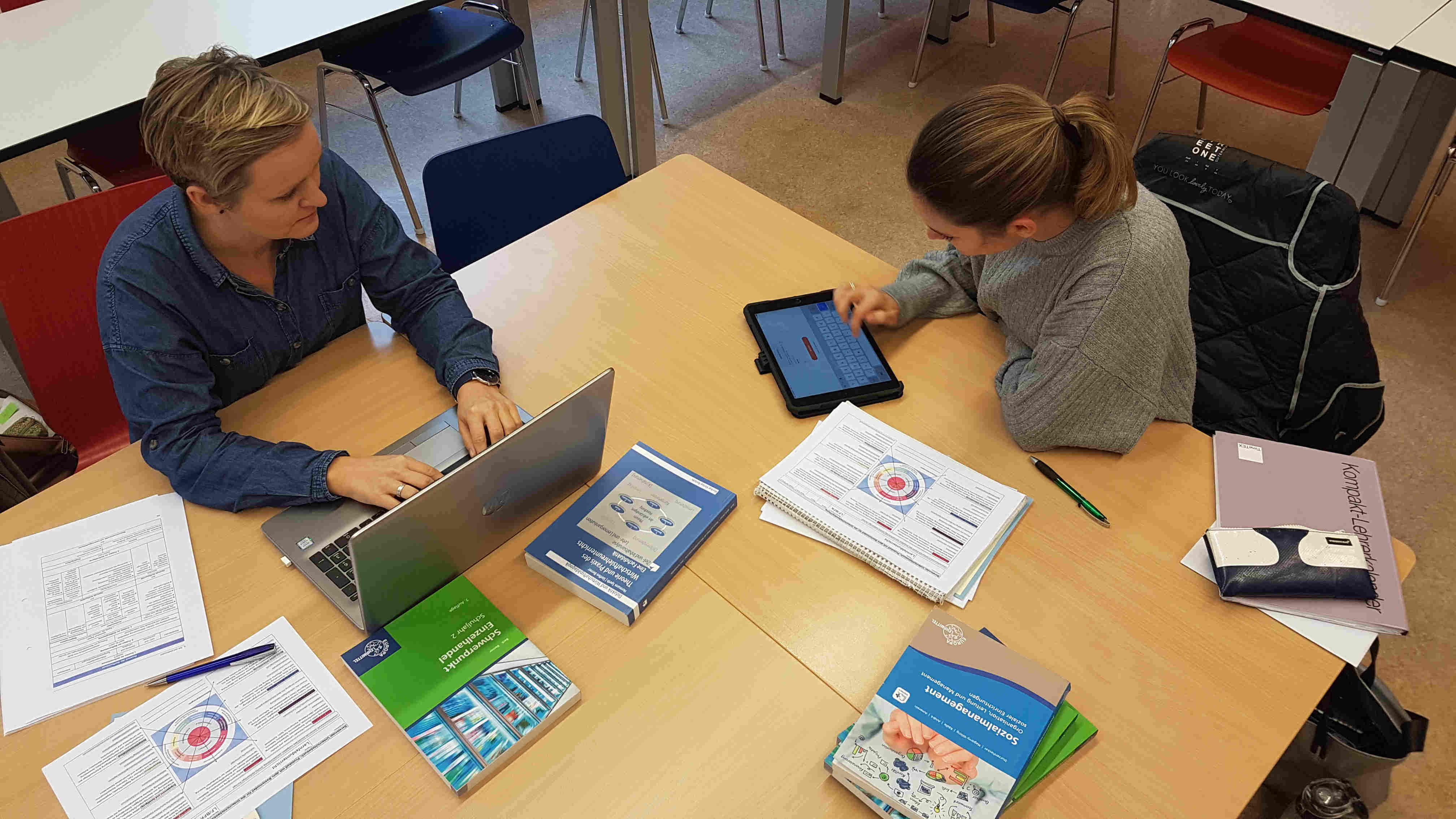 klassische Beratungssituation Auf dem Bild abgebildet findet sich eine klassische Beratungssituation einer Ausbilderin des Seminars Weingarten und einer Lehrkraft in Ausbildung. Auf dem Tisch liegend sieht man dabei diverse Referenzwerke der Fachdidaktik Wirtschaftswissenschaften, wie auch das Basismodell zur Unterrichtsreflexion des Landes Baden-Württemberg sowie mehrere digitale Endgeräte.